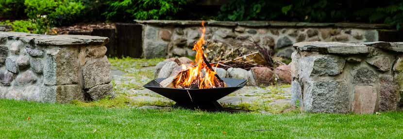A low wood-burning fire bowl beside a stone garden wall.