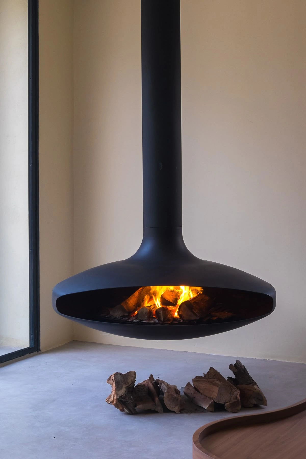 A black sculptural fireplace suspended over a concrete hearth.